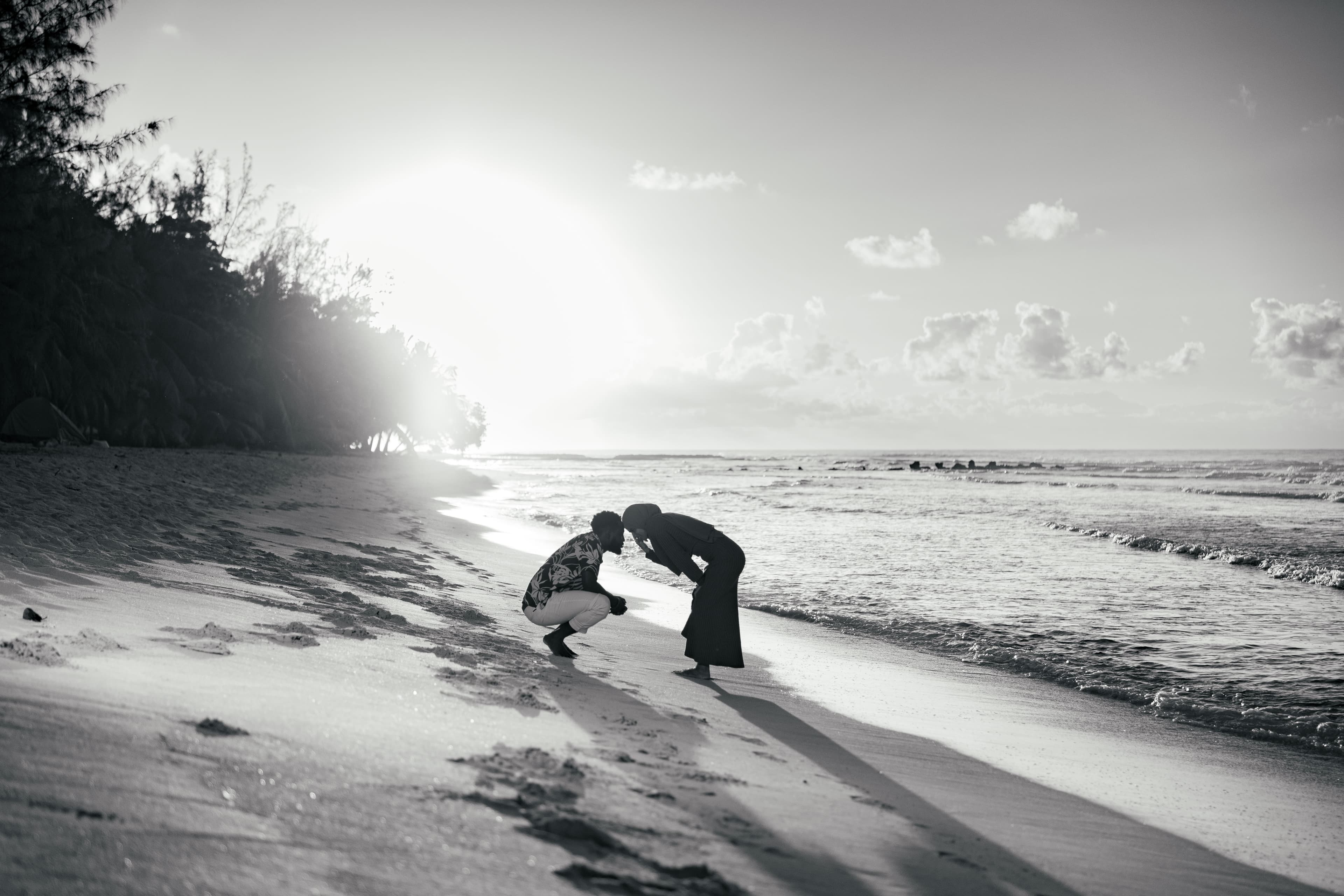 Couple touching foreheads on a sandy beach at sunset in a black and white photo.